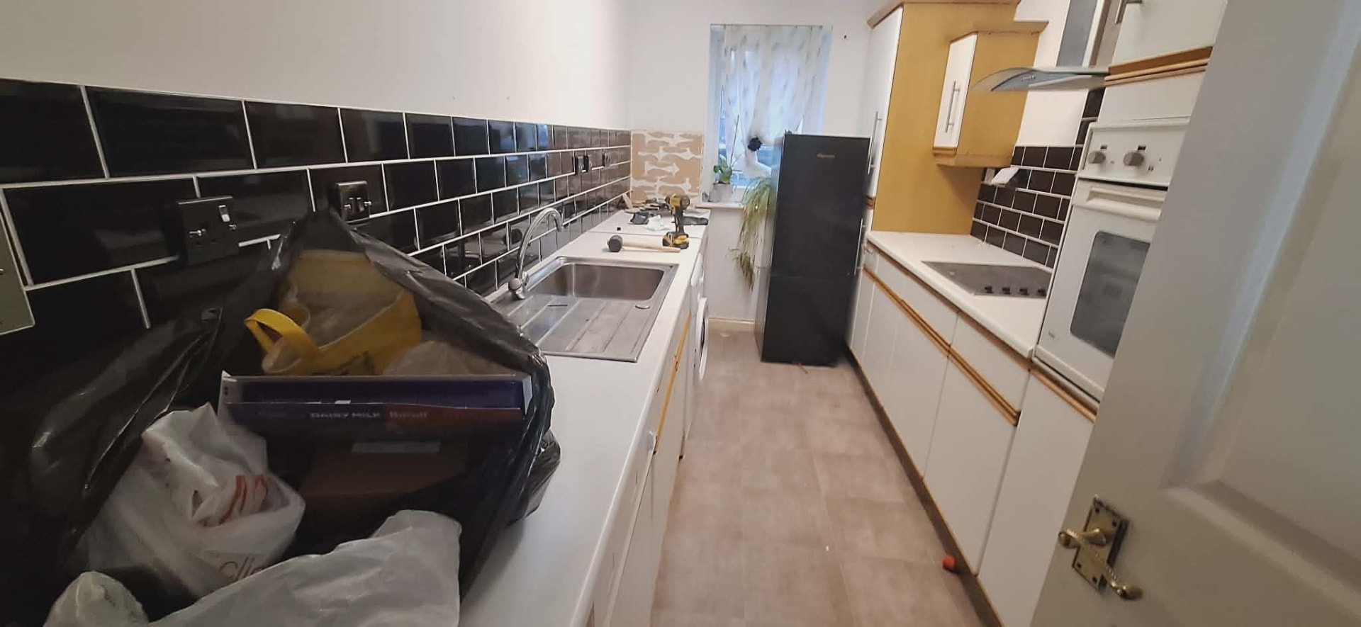 Dated galley kitchen with white units and black tiled splashback before renovation