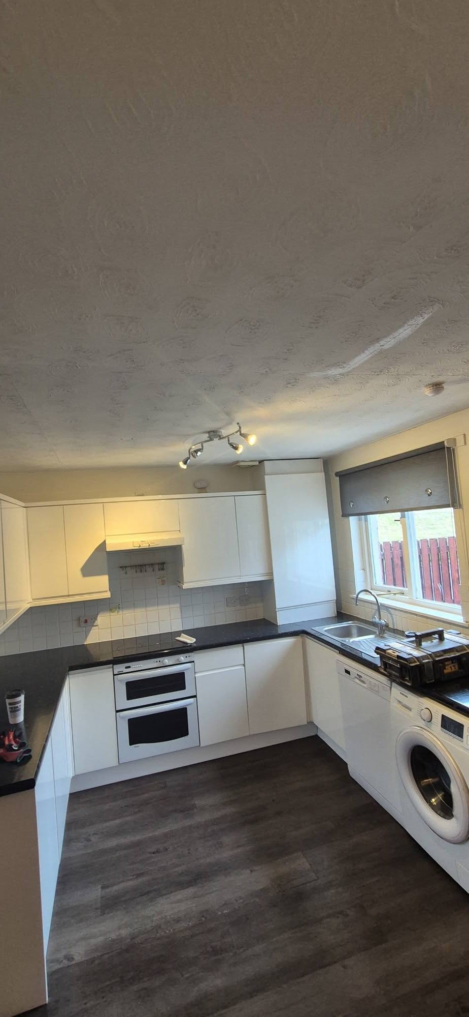 Old white kitchen with dark worktops, tiled splashback and textured ceiling before renovation