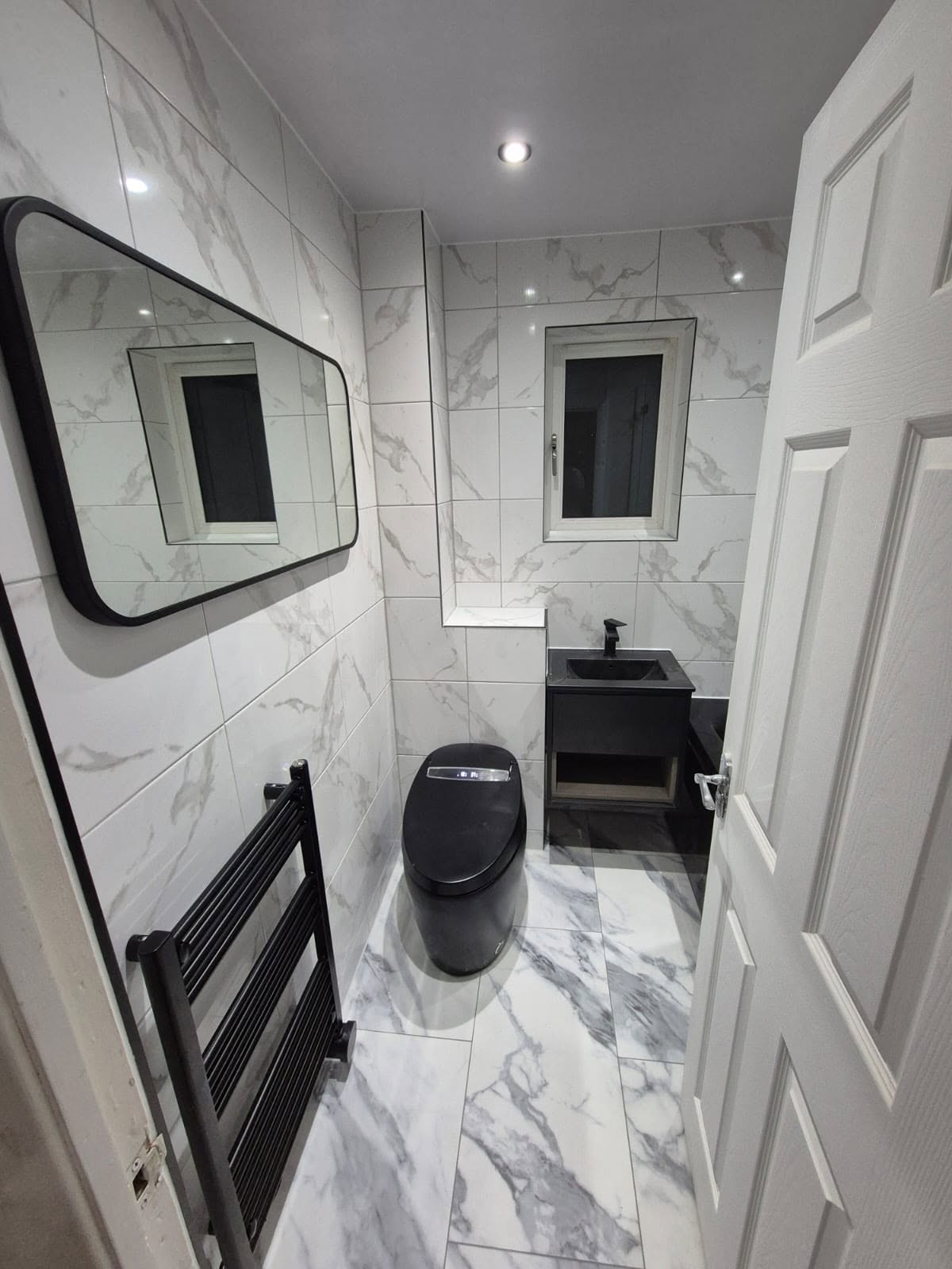 Finished bathroom with white marble tiling, black WC, black vanity and framed mirror