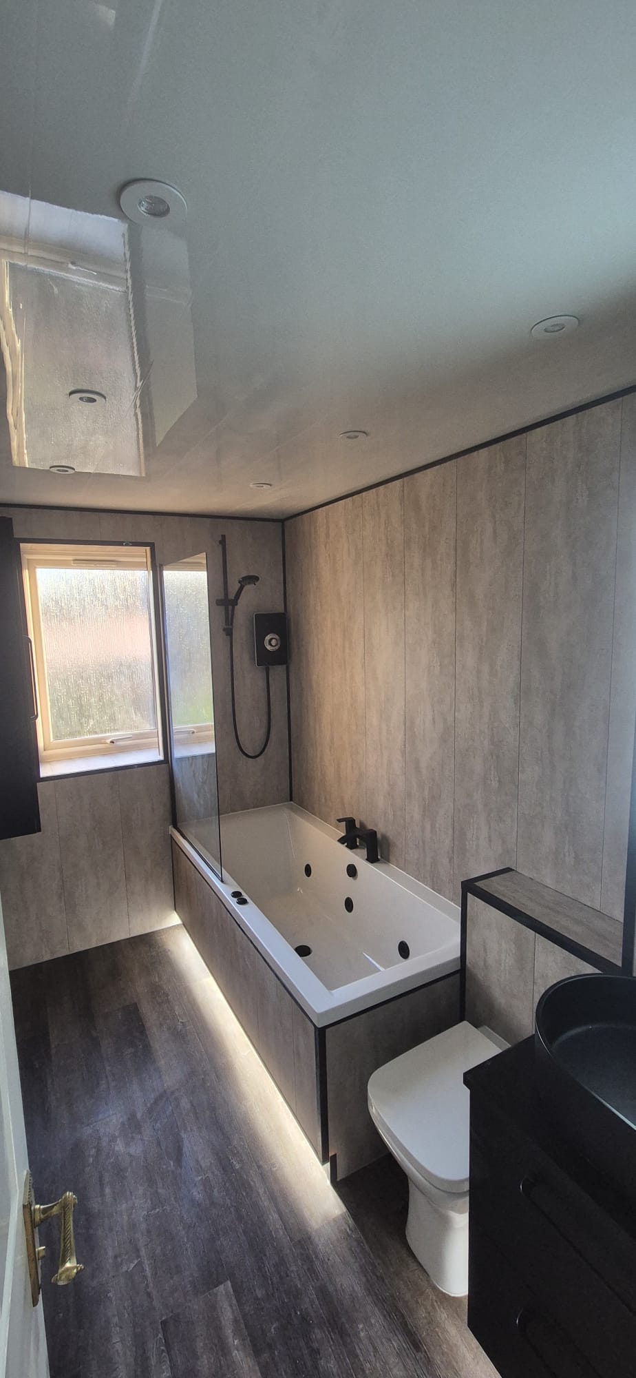 Finished bathroom with stone-effect panels, black fittings and LED lighting