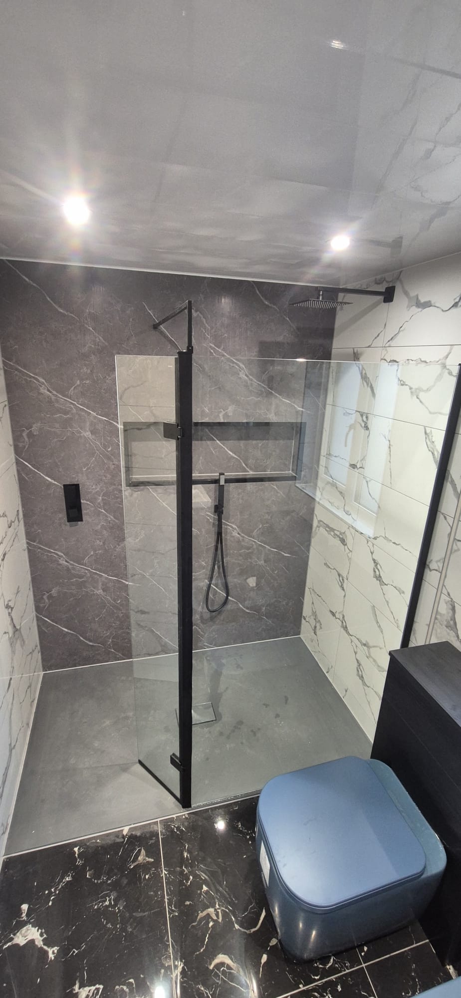 New bathroom with grey marble panels, black-framed walk-in shower and rainfall head
