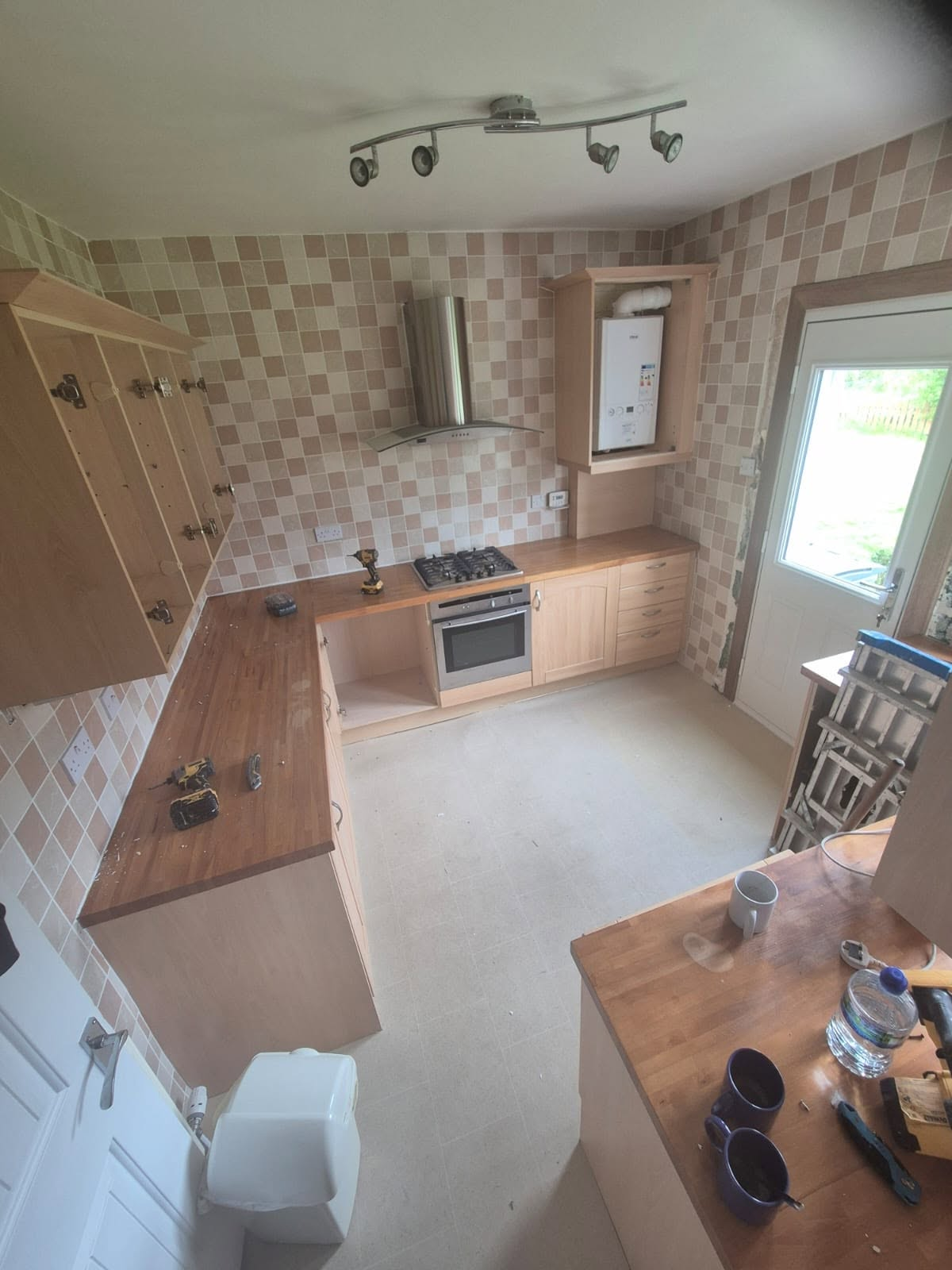 Old kitchen with beige tiled wallpaper and dated units stripped back before renovation