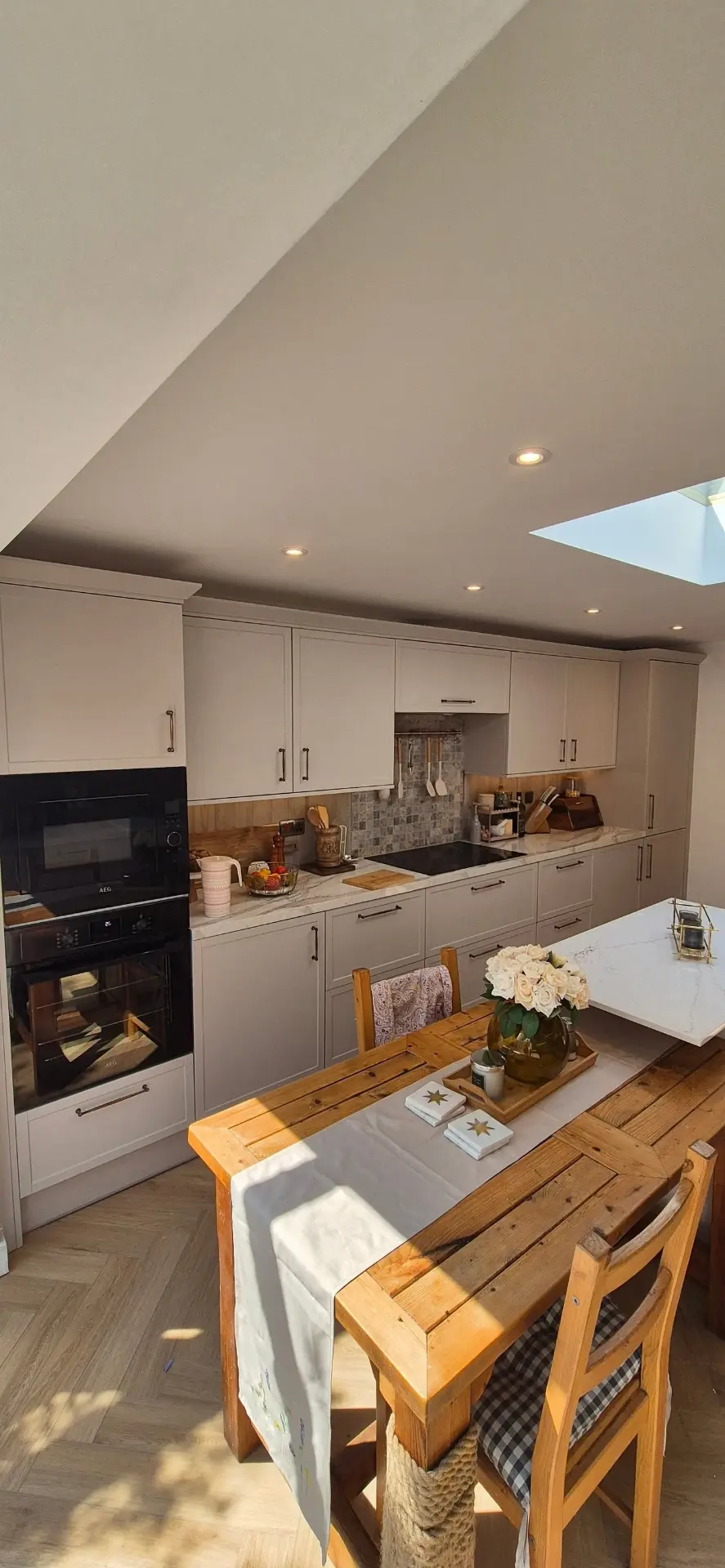 Finished kitchen with built-in ovens, mosaic splashback and dining table under the skylight
