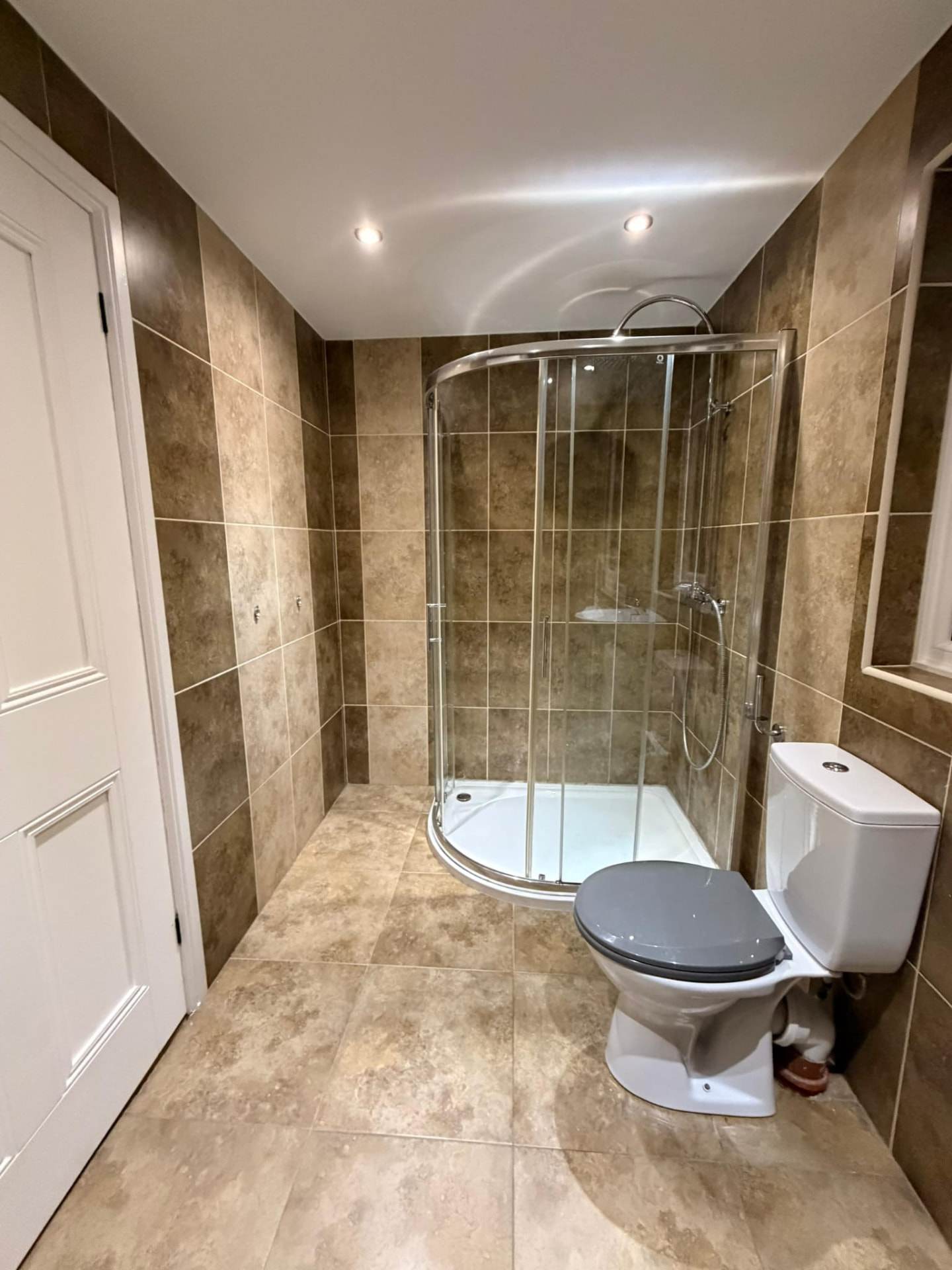 Old bathroom with brown tiling and a curved corner shower enclosure before renovation