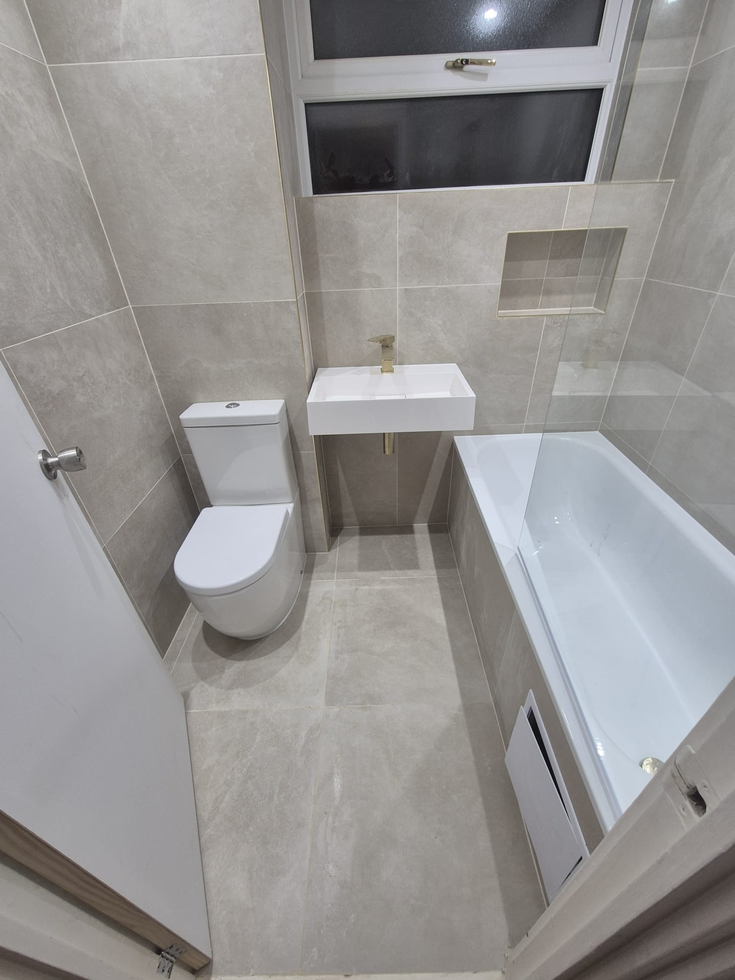 New bathroom with warm stone-effect tiling, wall-hung basin, gold tap and recessed niche