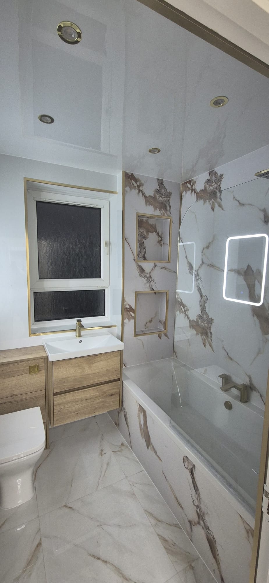 New bathroom with marble-effect panels, gold trims, oak vanity and glass bath screen